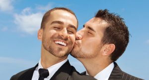 A man kisses his male partner on the cheek