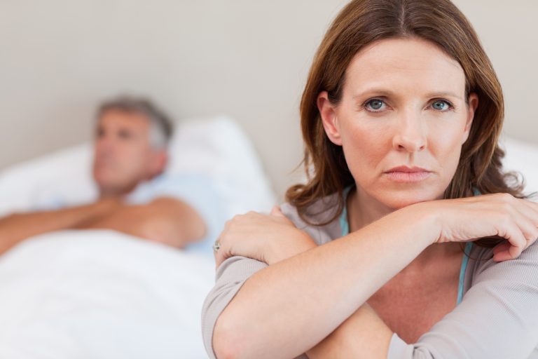 A forlorn woman in bed next to her male partner