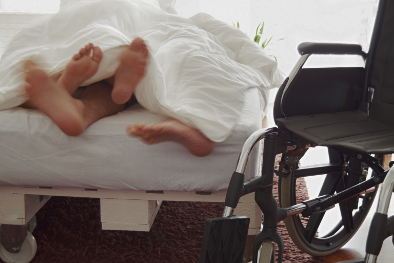 A happy couple is in bed with a wheelchair nearby