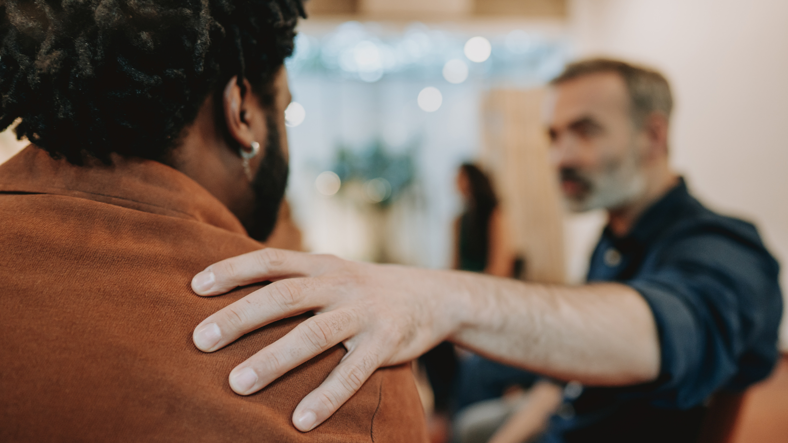 A man consoles another man by putting a hand on his shoulder
